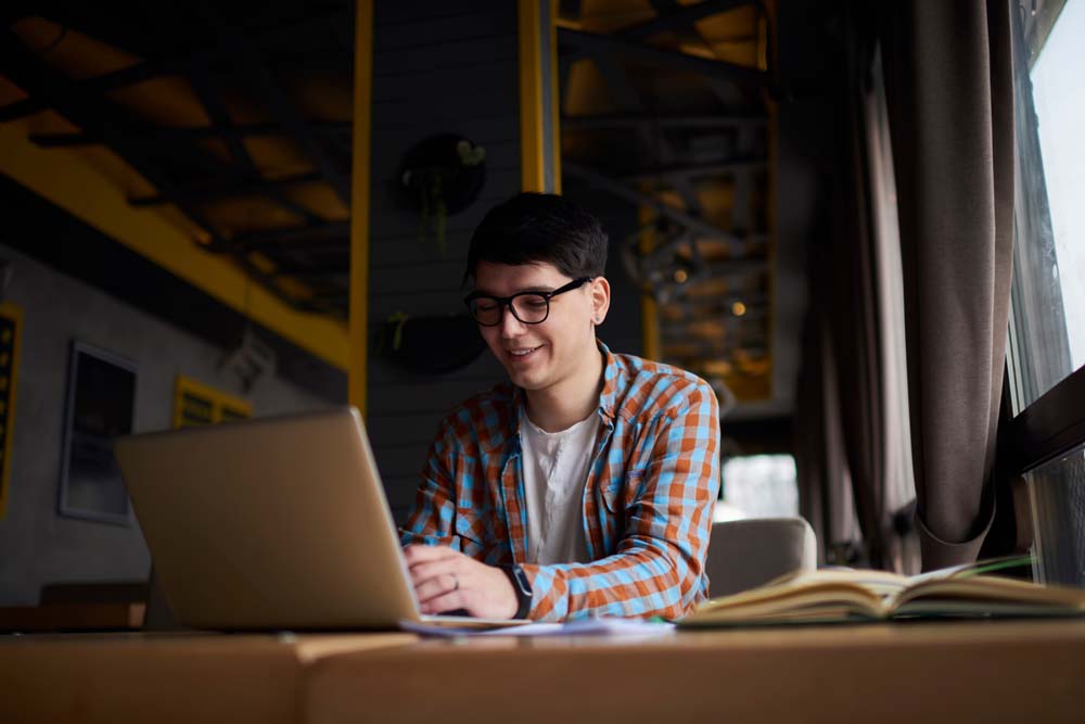 Young,Millennial,Male,Sitting,At,Table,Front,Open,Laptop,Computer